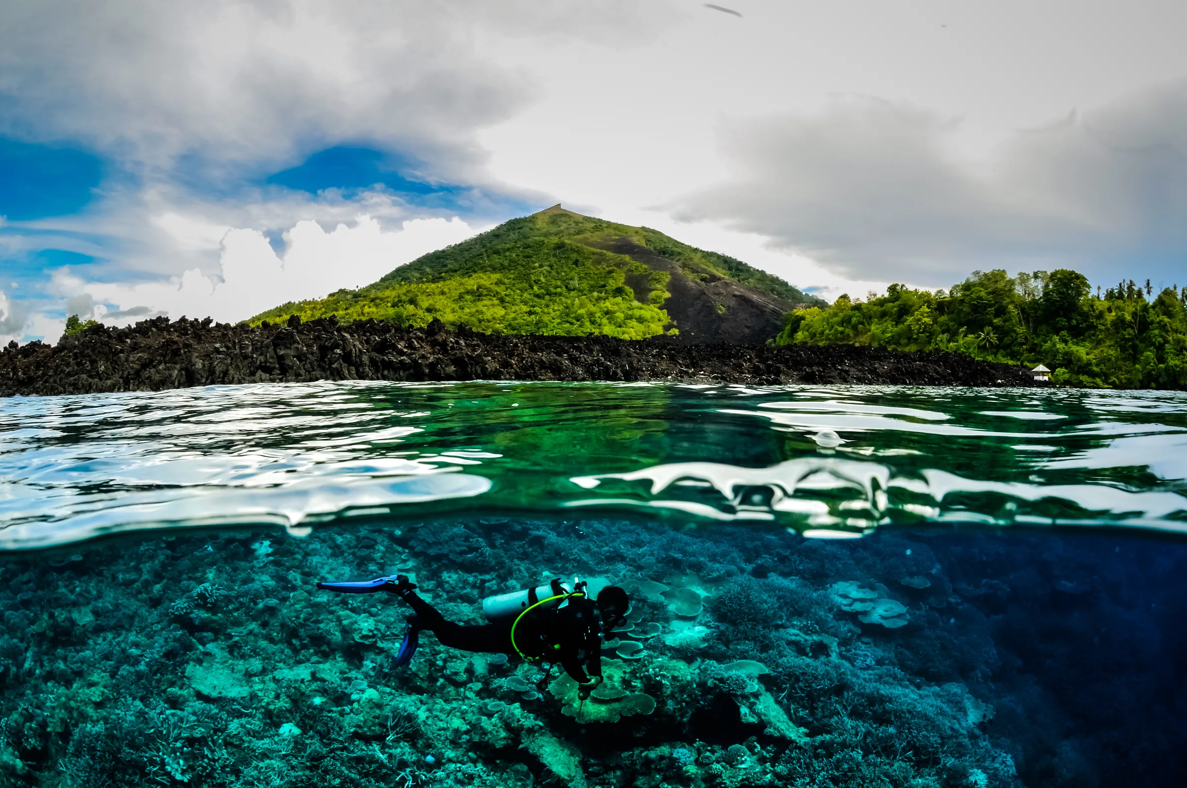 A snorkeler over the reef, a green volcano above the surface